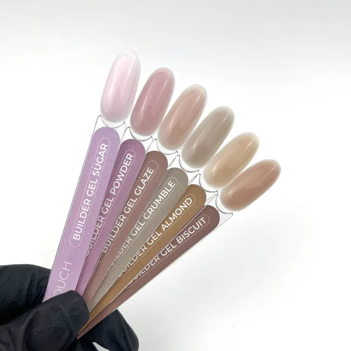 Set of TOUCH Builder Gel Powder samples in various shades held by a gloved hand on a white background.