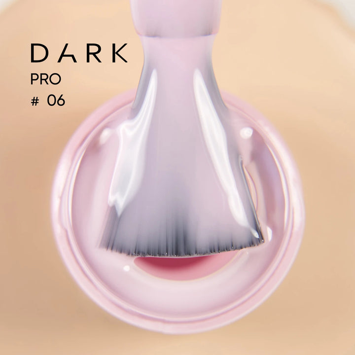 Close-up of a nail polish brush dipped in glossy light pink gel, labeled Dark Pro 