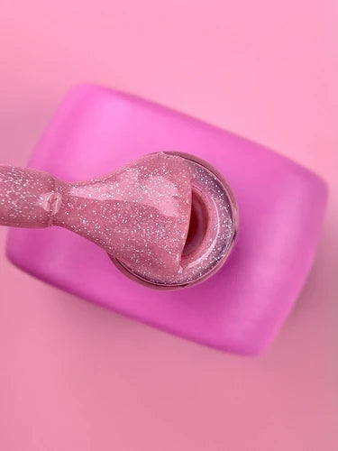 Bottle of pink glitter gel nail polish with brush, on pink background