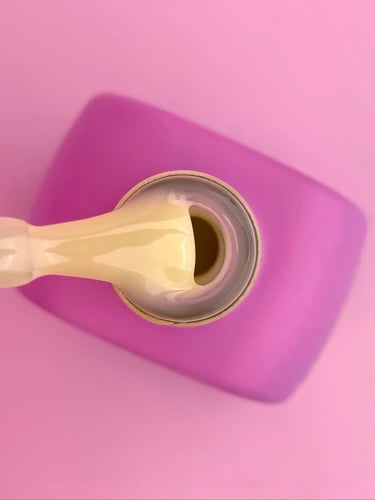 Yellow UV gel nail polish brush over open bottle on pink background