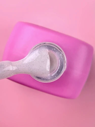 Clear glitter UV gel on nail brush, pink container, manicure supplies background