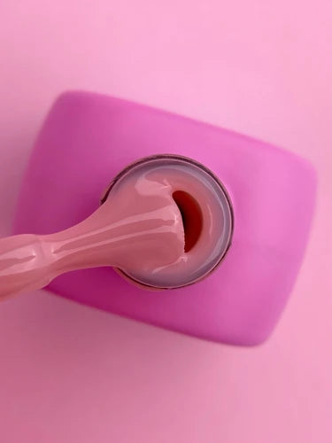 Open pink UV gel nail polish jar with applicator on pink background