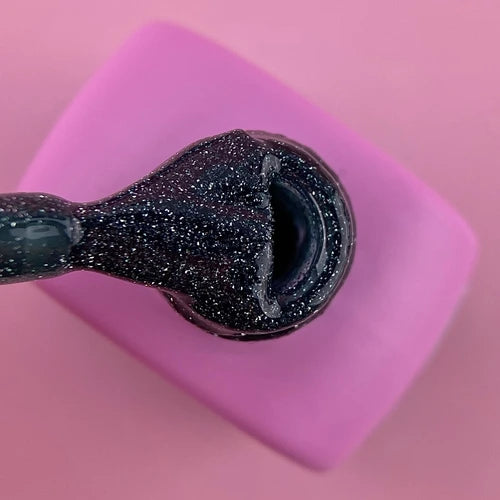 Black glitter gel nail polish on brush over pink background
