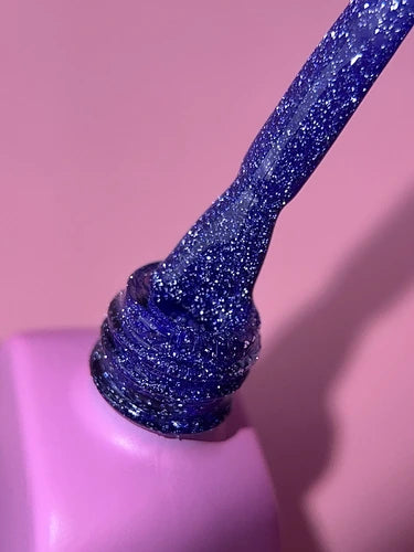 Blue glitter gel nail polish bottle with brush on pink background