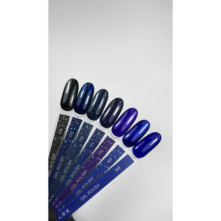 Six gel nail polish color samples on applicator sticks, arranged in a fan shape on a light gray background. The shades range from dark gray and navy with glitter to deep purple and royal blue.