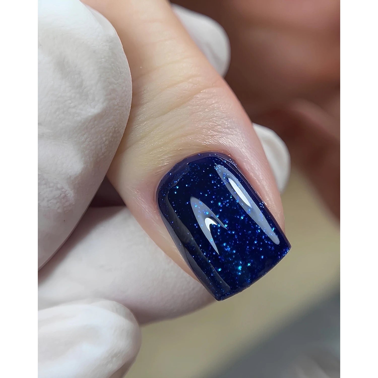 Close-up of fingernail with dark blue glitter gel polish, manicure detail