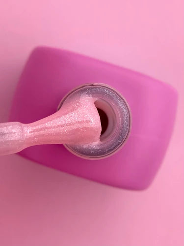 Shimmery light pink nail polish bottle with brush on a pink background