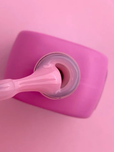 Open pink nail gel polish jar with applicator brush on a pink background
