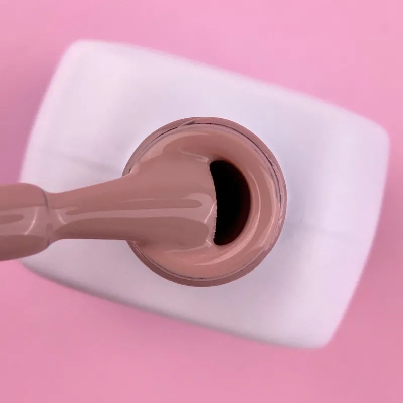 Nude gel nail polish bottle with brush against pink background