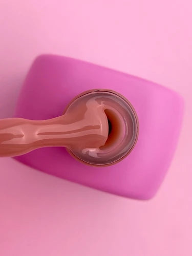 Nude pink gel nail polish in open bottle with applicator on pink background