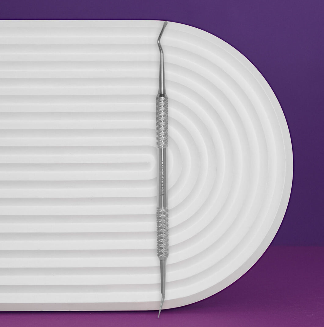 Double-ended stainless steel cuticle pusher nail tool on white textured background with purple base.