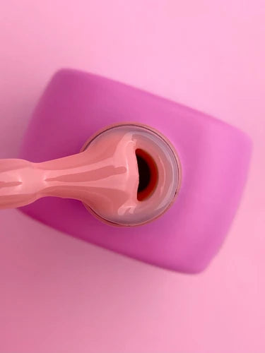 Close-up of pink gel nail polish bottle with brush on pink background