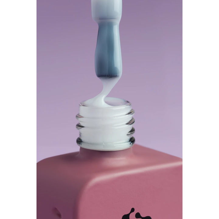 Close-up of white UV gel polish on brush above a pink bottle, manicure product