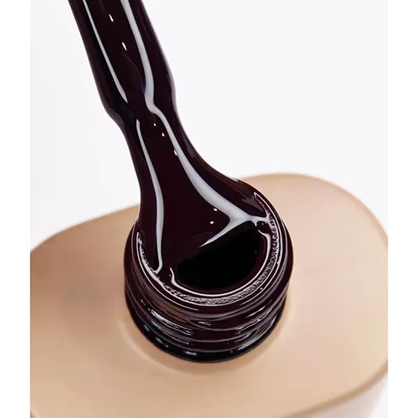 Dark burgundy gel nail polish on applicator brush above open bottle