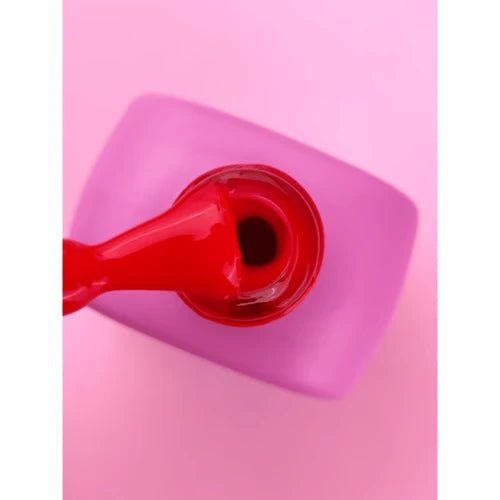 Red gel nail polish being lifted from a pink bottle on a pink background