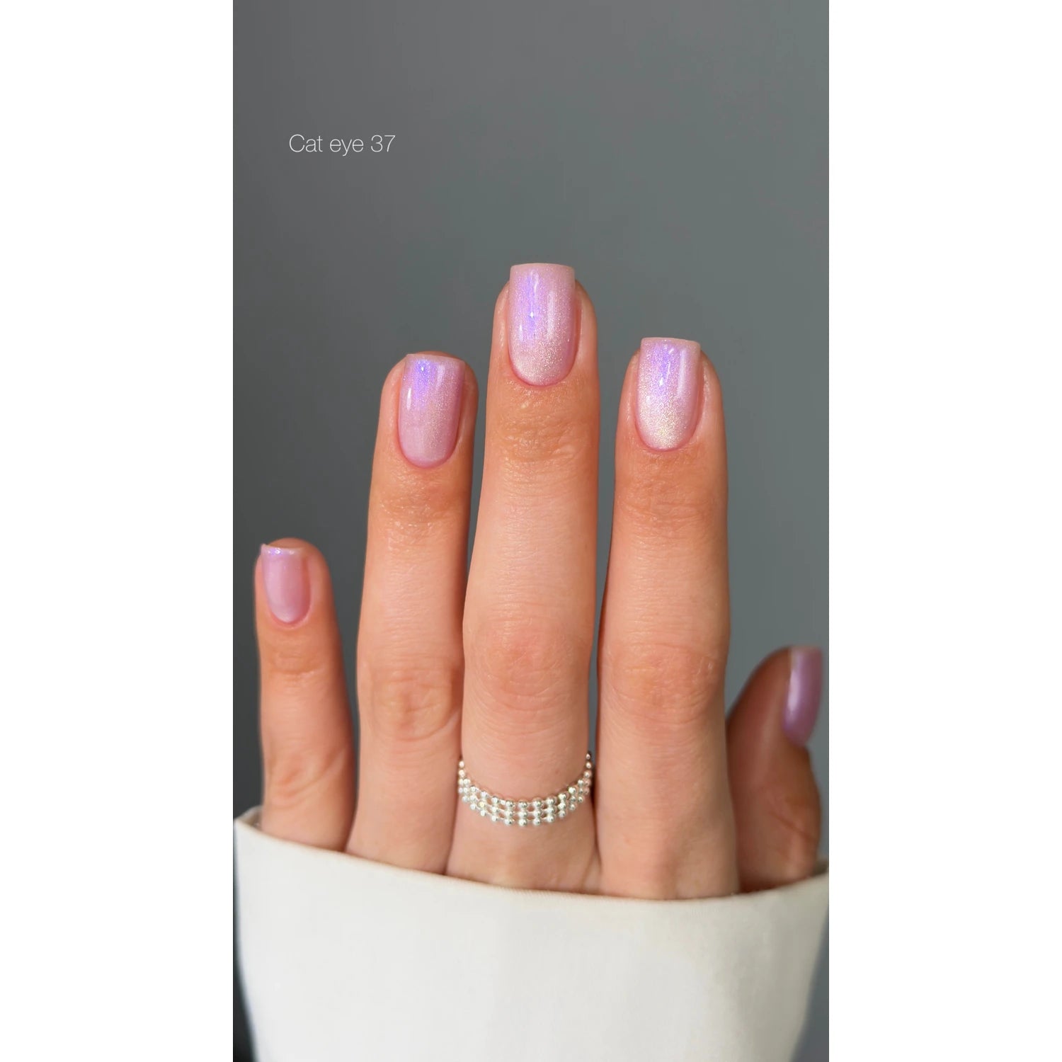 Hand with light pink cat eye gel nail polish and shimmery manicure, silver ring