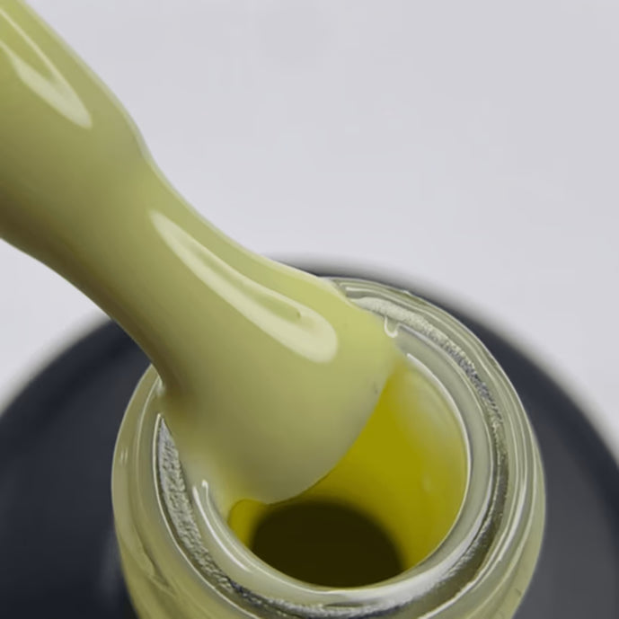 Close-up of brush with light yellow gel nail polish over open bottle