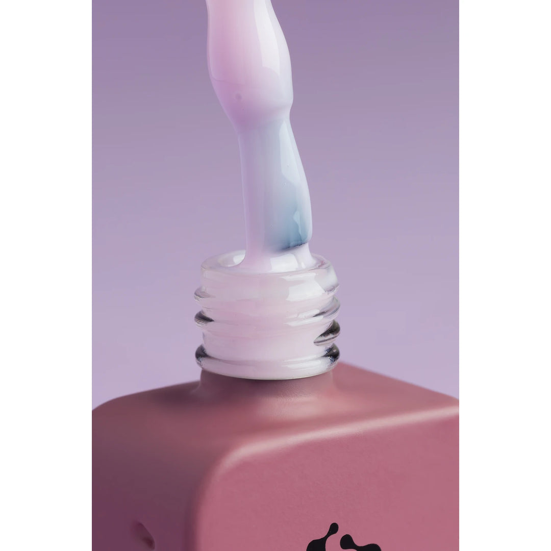 Close-up of pastel pink gel nail polish bottle and brush on purple background