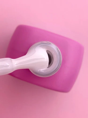 White UV gel nail polish on brush above pink bottle, manicure product on pink background
