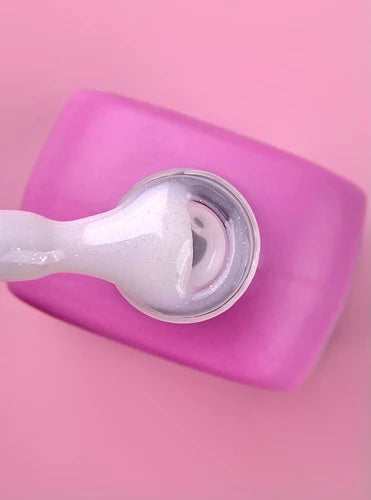 Shimmery white UV gel polish on applicator with pink jar, manicure supplies
