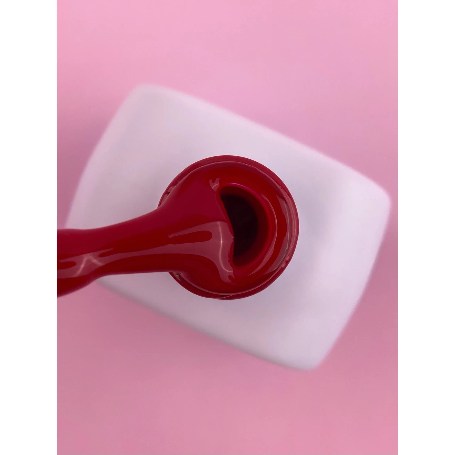 Red gel nail polish brush over open bottle, pink background, manicure supplies