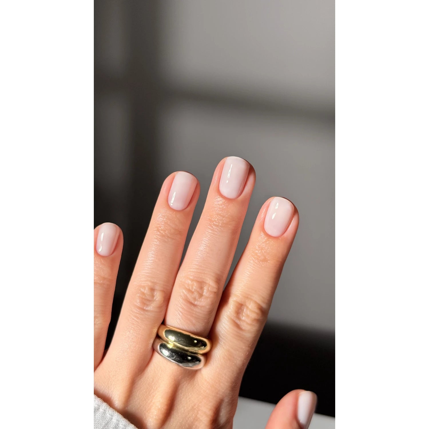 Hand with short, natural nude gel polish manicure and gold and silver rings