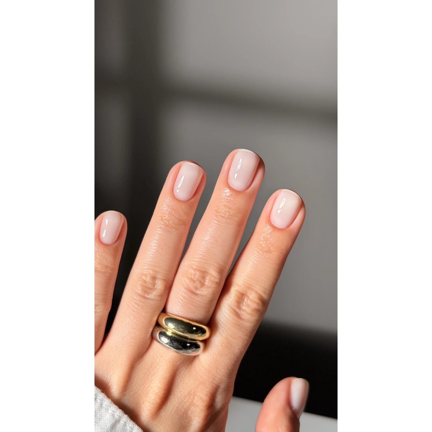 Hand with natural pink gel manicure, short square nails, gold and silver rings