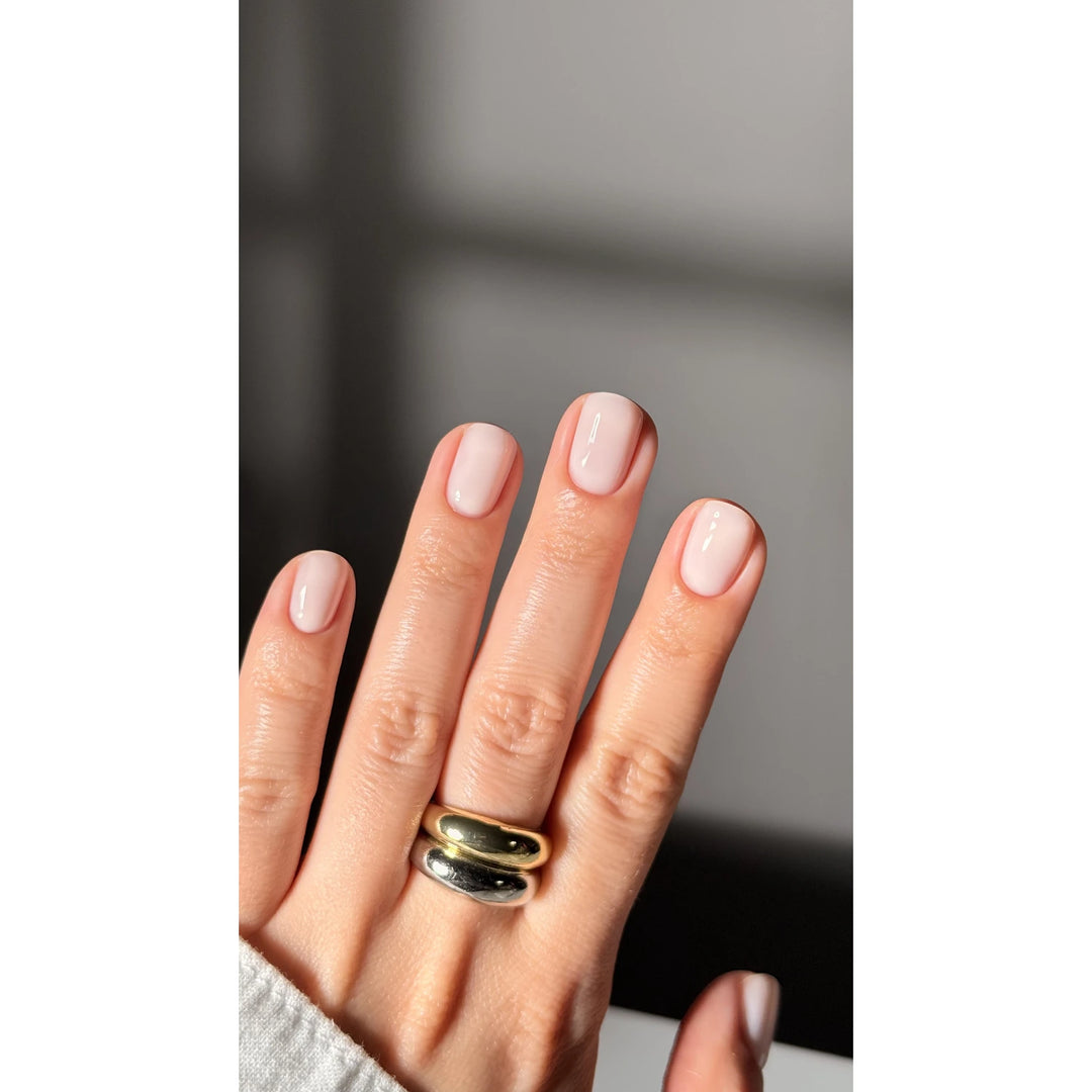 Hand with short, glossy light pink gel nails and gold silver chunky rings, manicure concept