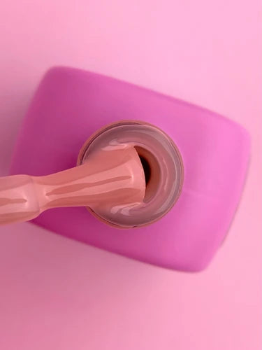 Pink nude gel nail polish bottle with brush on pastel pink background
