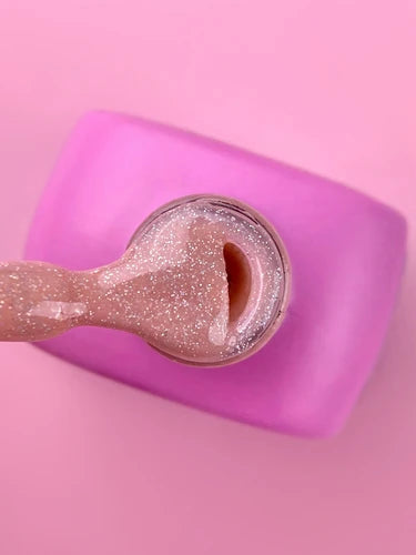 Open jar of pink glitter UV gel nail polish with applicator on a pink background