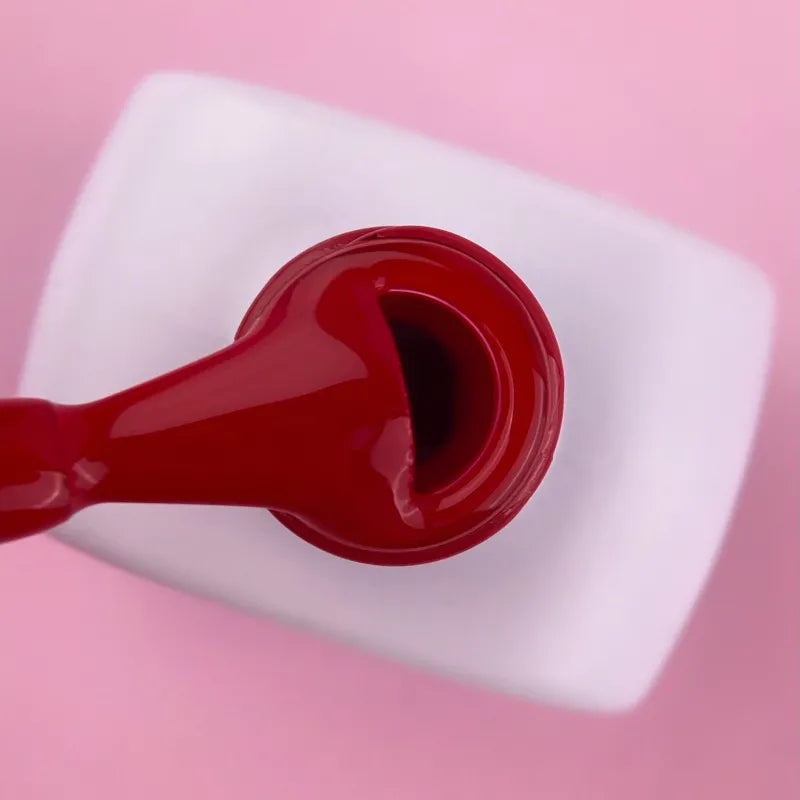 Red gel nail polish bottle with brush on a pink background, manicure product