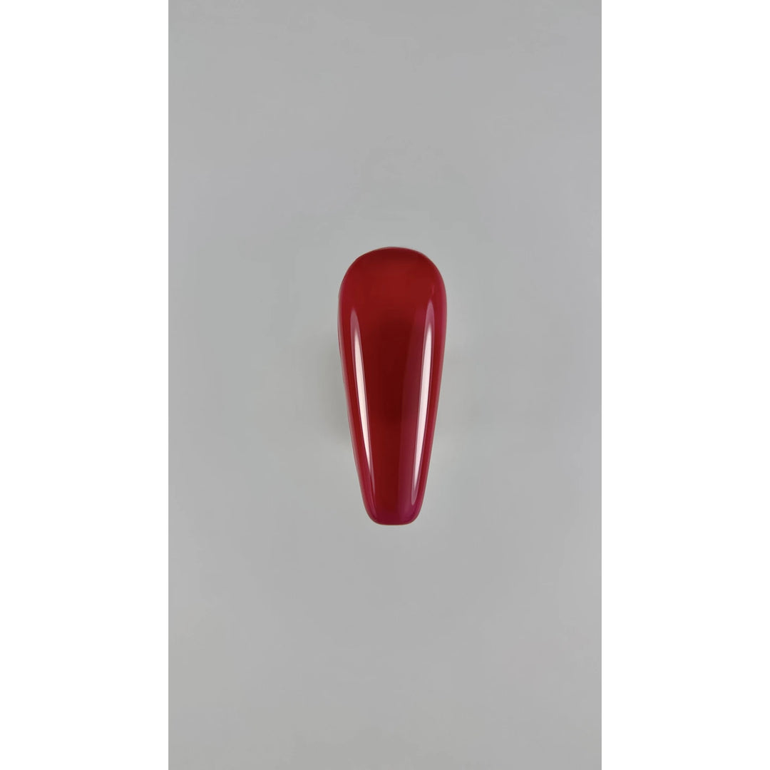 Glossy red nail polish swatch on artificial nail tip, manicure product display