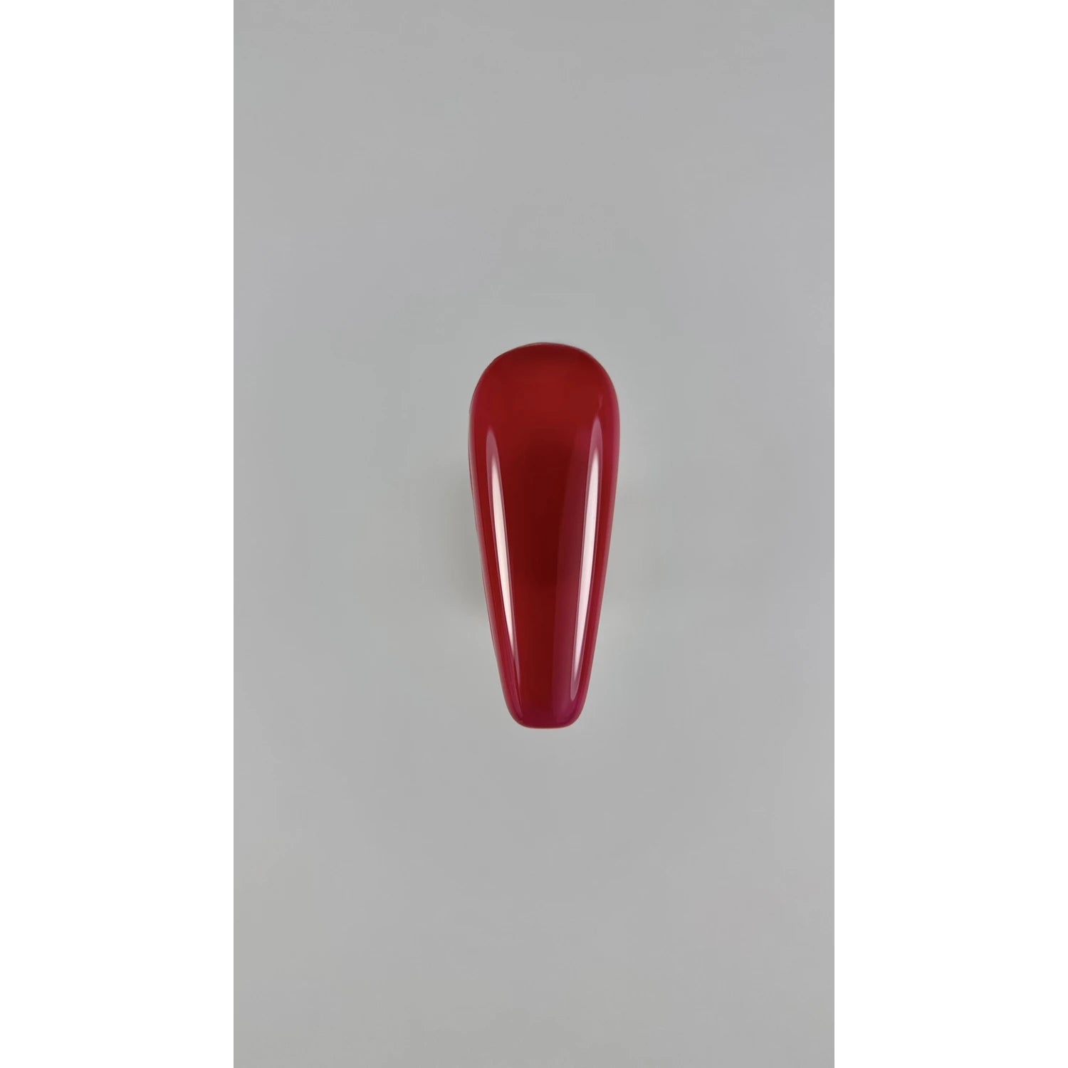 Glossy red nail polish swatch on artificial nail tip, manicure product display