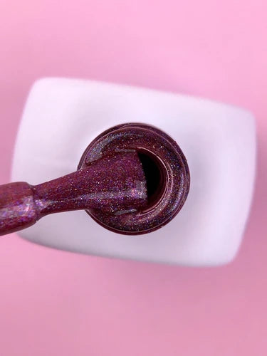Shimmery cat eye gel nail polish brush over an open bottle on a pink background
