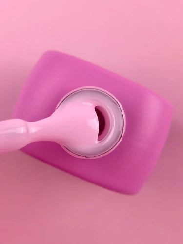 Pink UV gel nail polish bottle with applicator on a pastel pink background