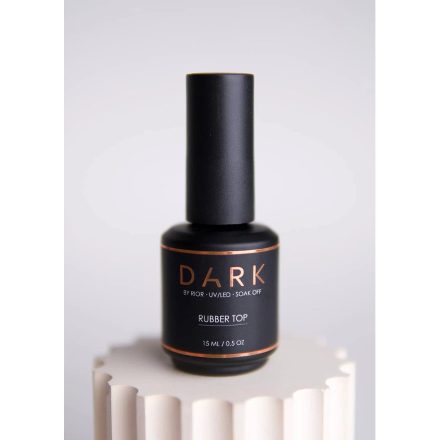 Black bottle of DARK Rubber Top UV/LED soak off nail gel, 15ml, on neutral pedestal