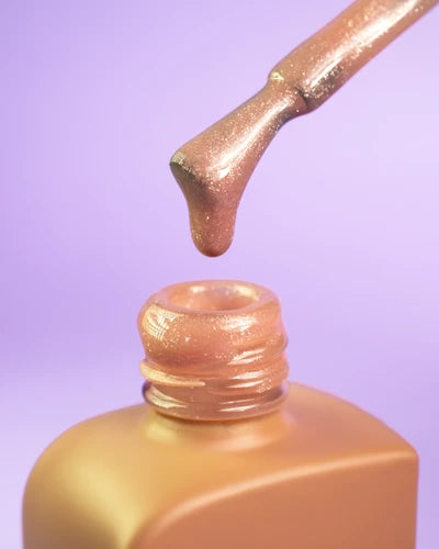 Shimmery nude gel nail polish in open bottle with brush, purple background