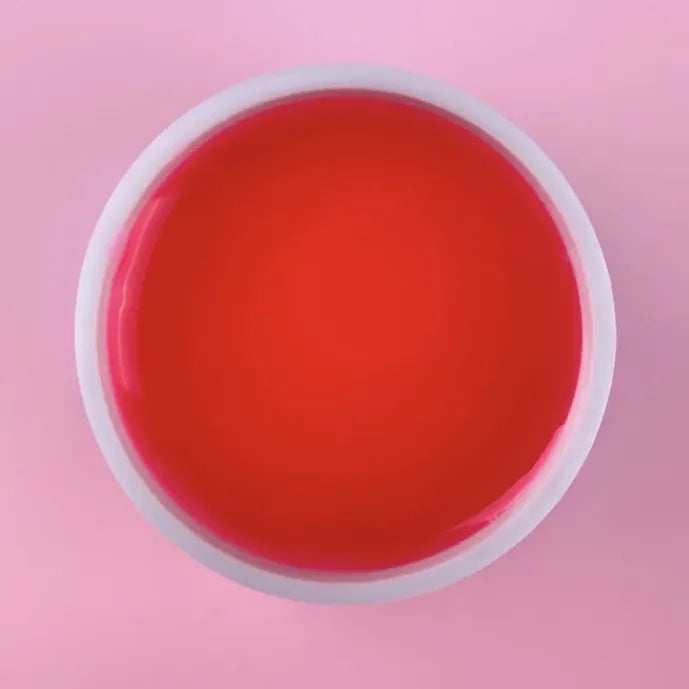Open jar of pink builder gel for nails on a pastel pink background