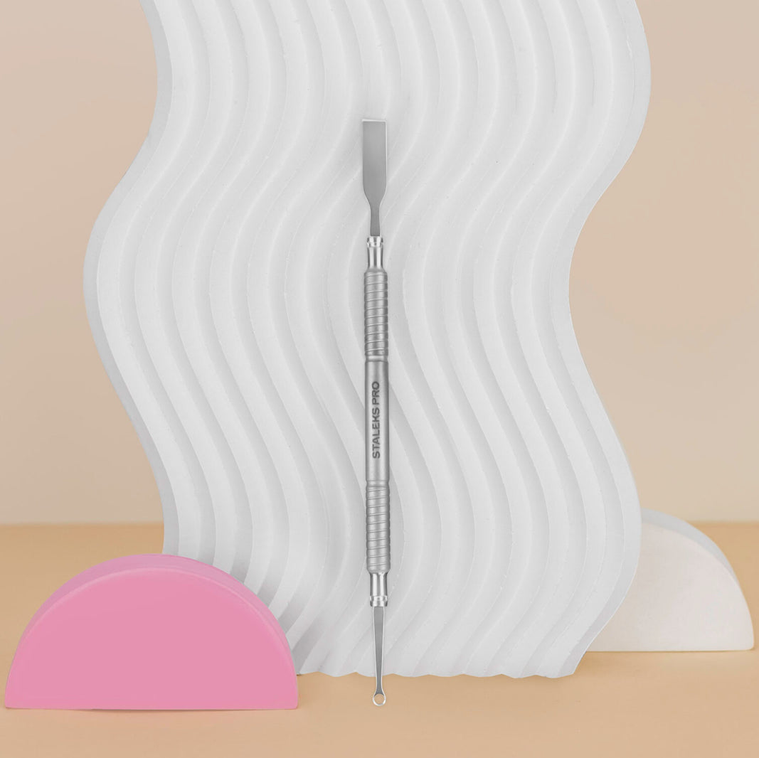 Stainless steel nail cuticle pusher and cleaner tool on wavy white display, manicure accessory
