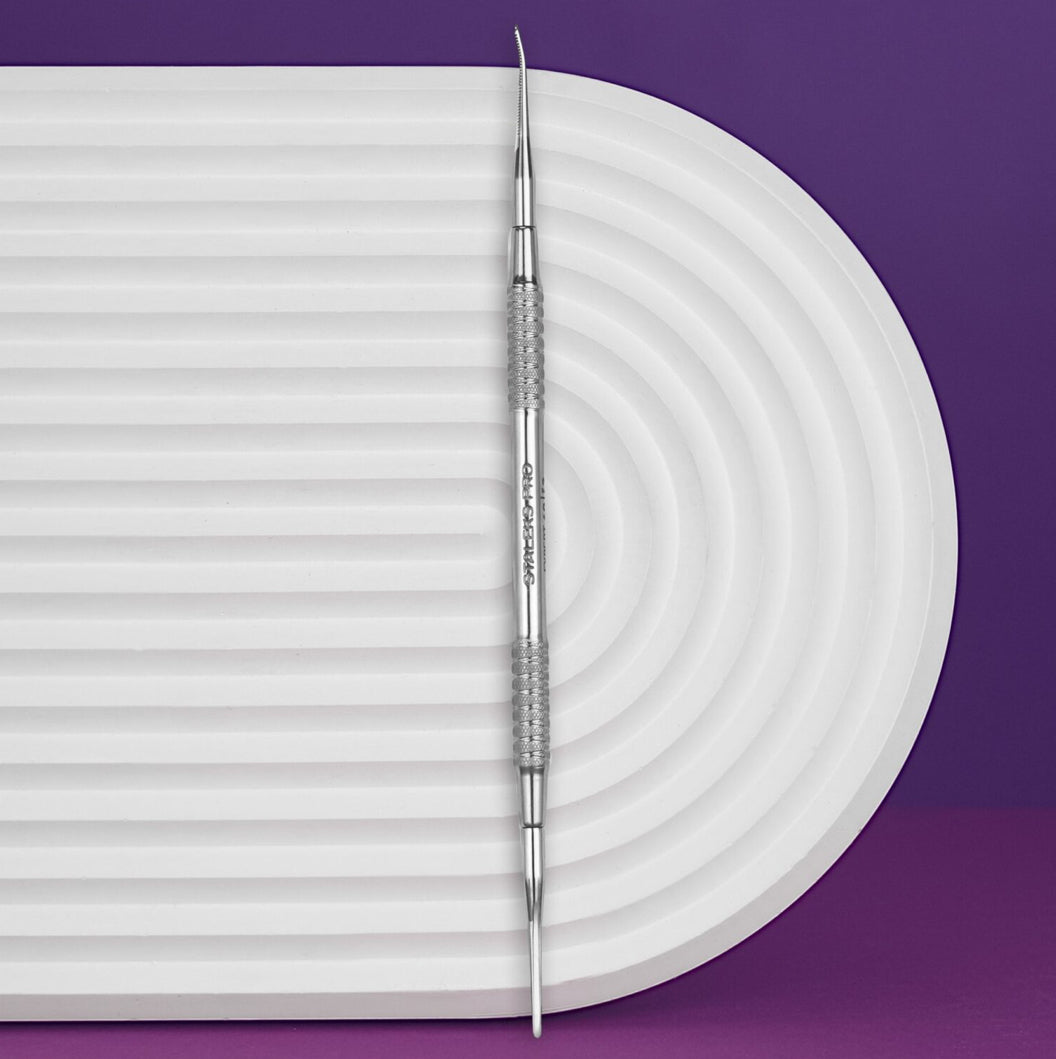 Double-ended stainless steel nail art tool on white textured surface, purple background