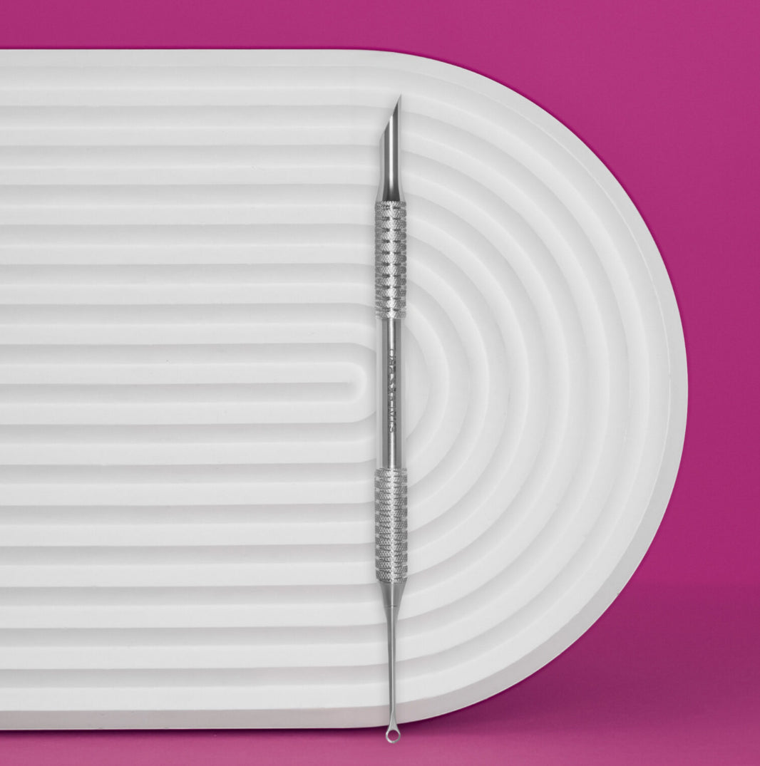Stainless steel double-ended manicure cuticle pusher on white textured tray, pink background