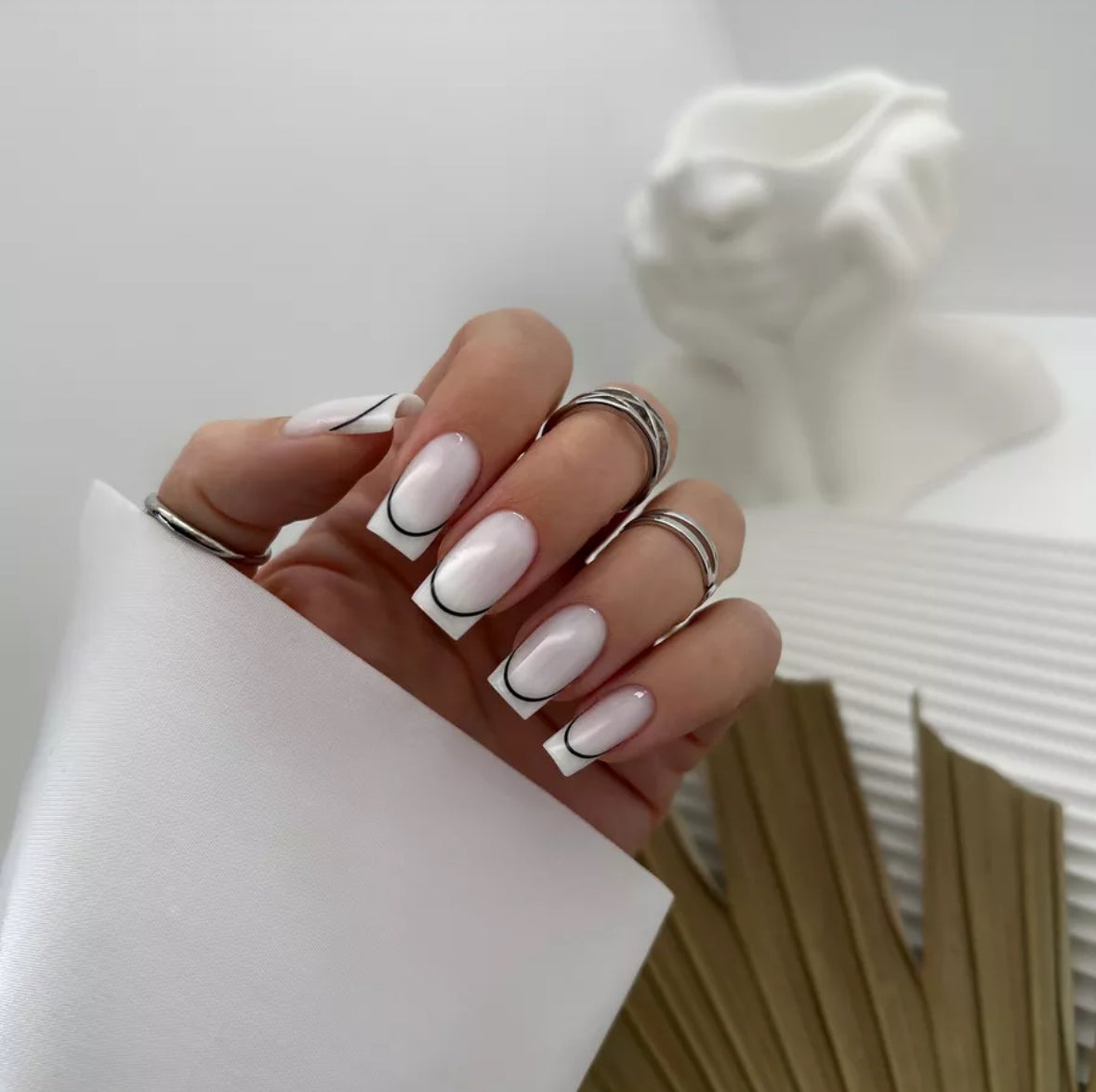 Hand with French manicure, white gel nails and black line accents, wearing silver rings