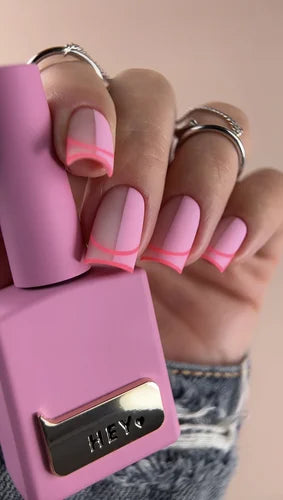 Hand with pink matte nail polish and geometric neon pink tips, holding matching polish bottle
