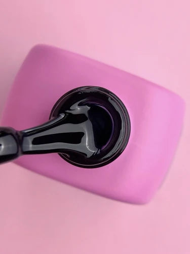 Close-up of black gel nail polish bottle with brush on pink background, manicure product
