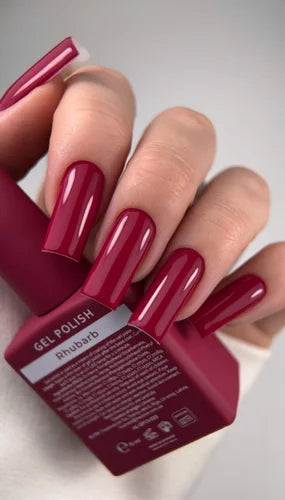 Woman fingers with red nails holding red gel polish bottle.