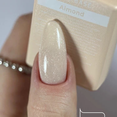Hand with almond-shaped nail painted in shimmery nude gel polish, holding Almond nail polish bottle