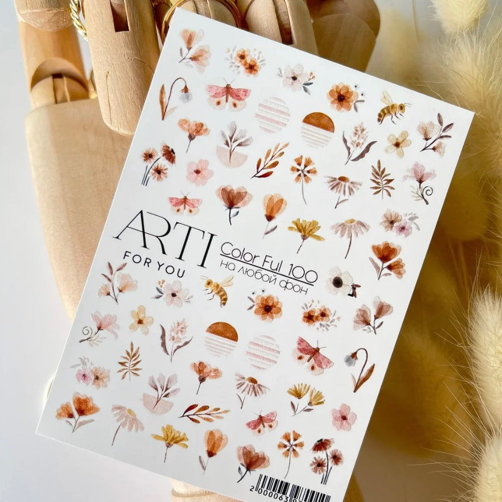 Sheet of floral nail art stickers with pastel flowers, butterflies, and bees held by a wooden hand