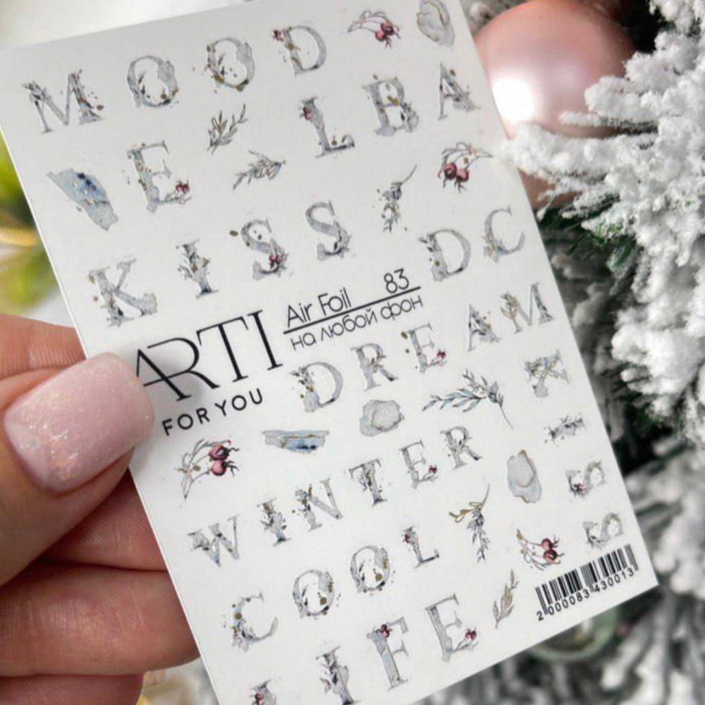 Sheet of decorative nail art stickers with letters and winter designs held by manicured hand