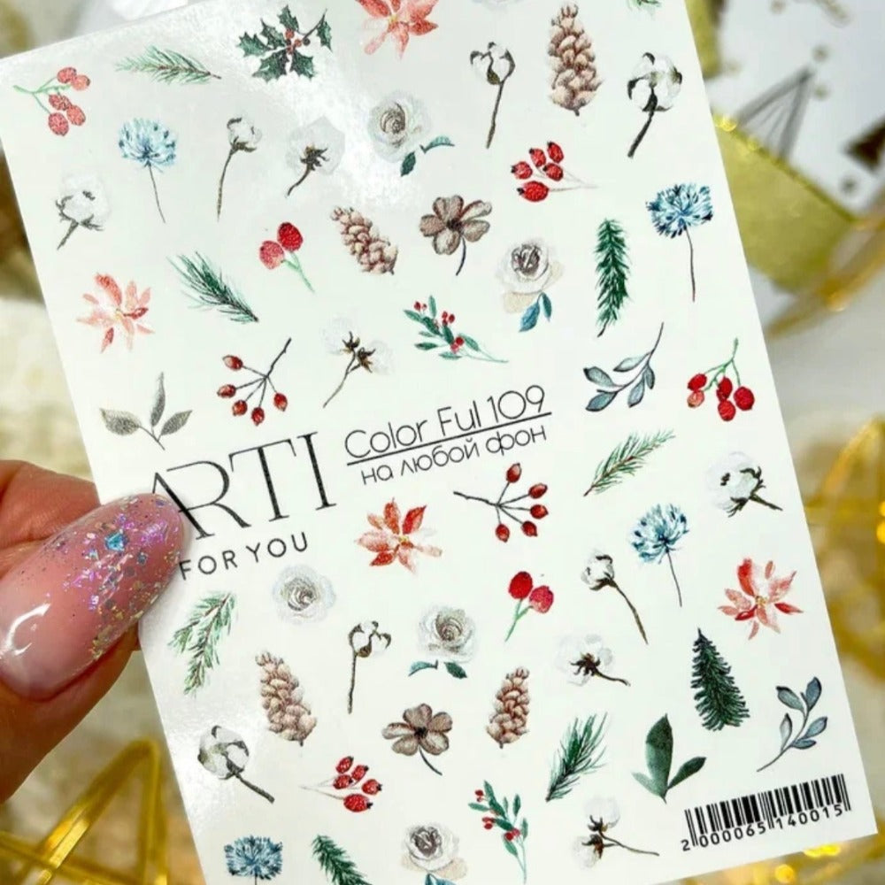 Floral nail art stickers sheet with botanical and berry designs held by a hand with manicured nails