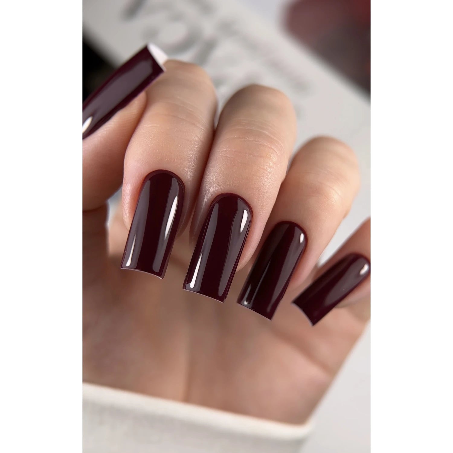 Hand with long square-shaped nails painted glossy dark burgundy gel polish